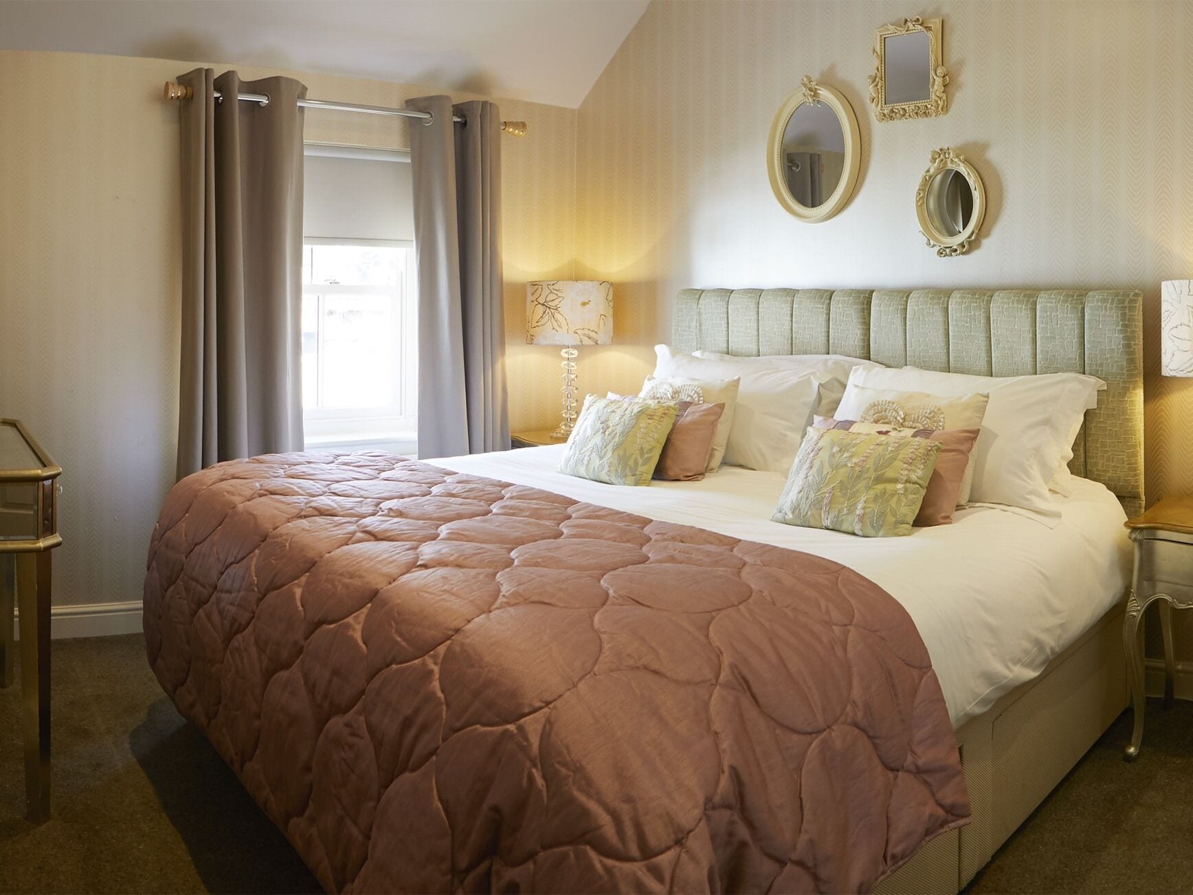 A neatly made bed with a brown quilt, a bedside lamp, and a nightstand with a mirror.