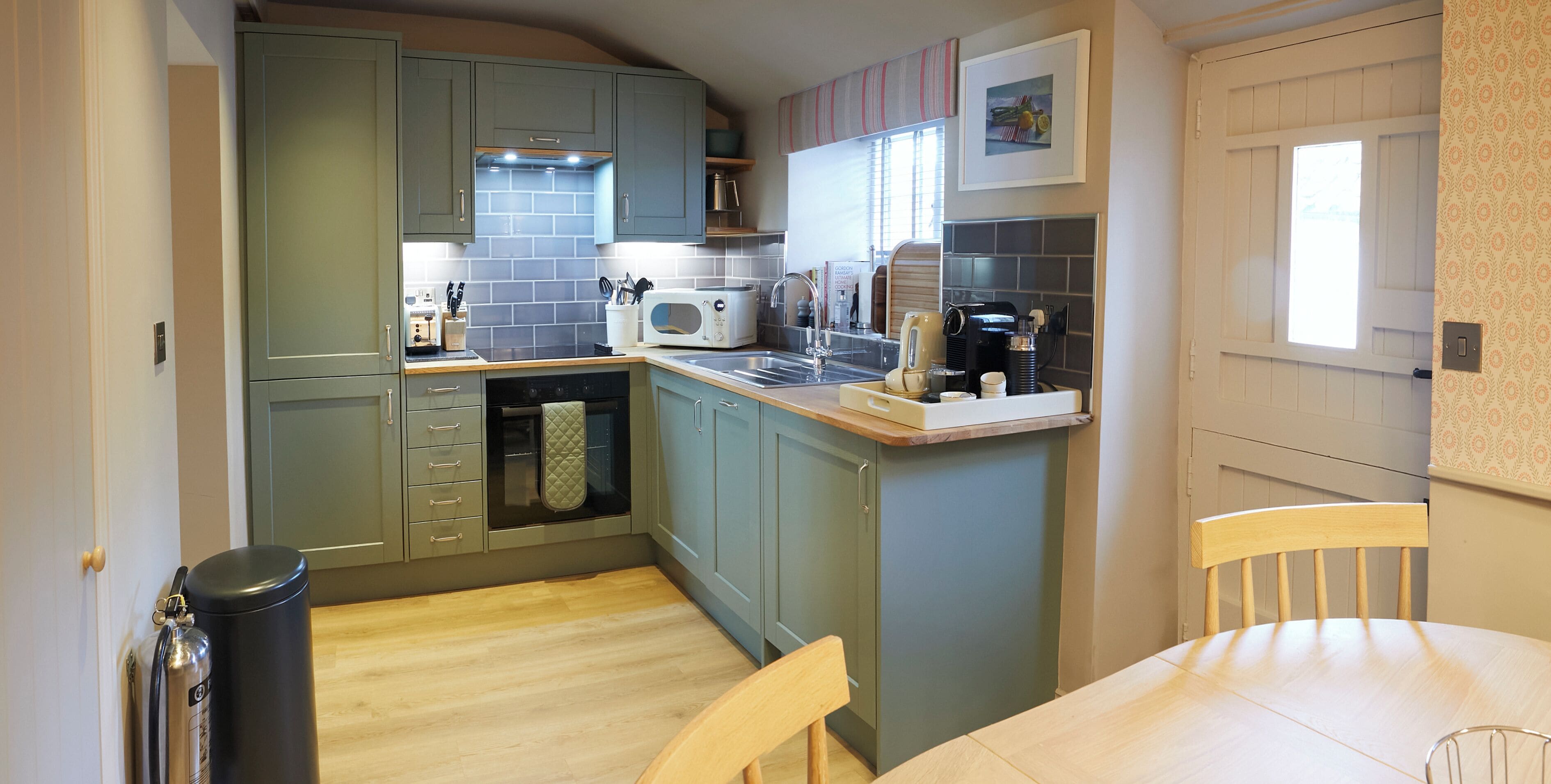A compact kitchen with teal cabinets, a microwave, a coffee maker, and a small dining table.