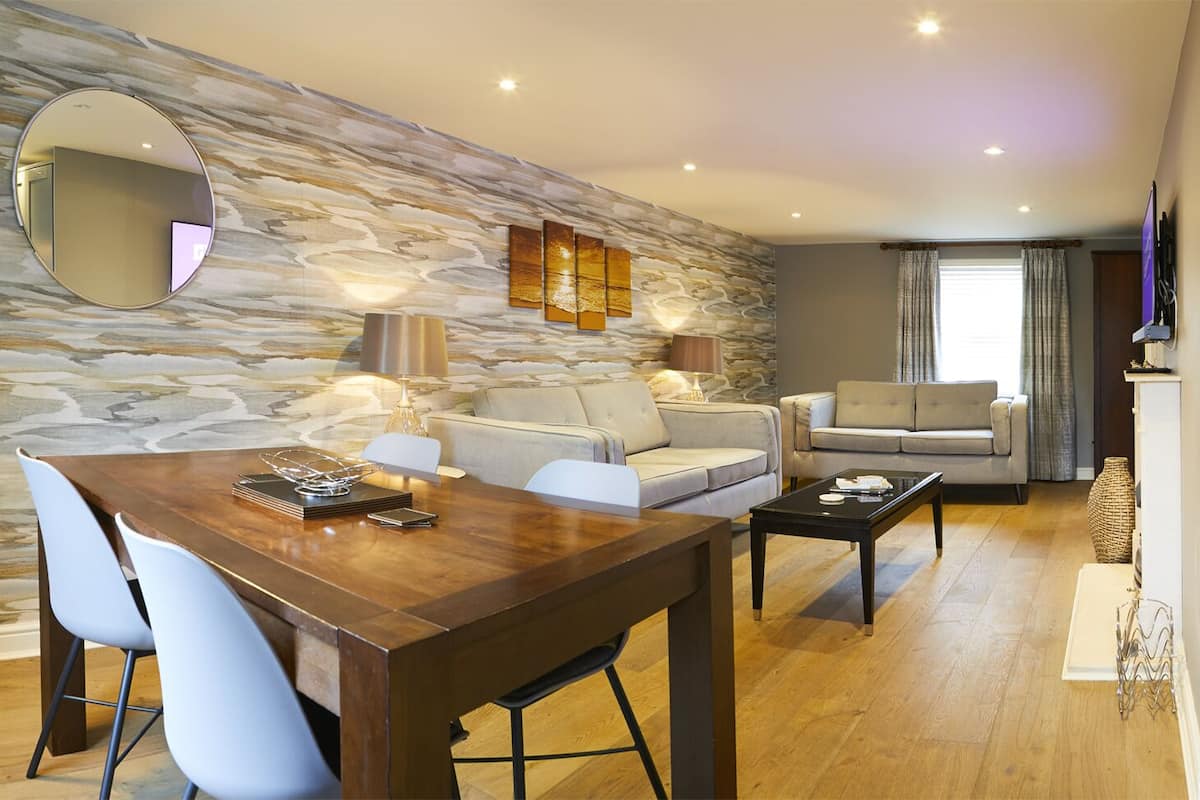 Een moderne woonkamer met een stenen muur, een eettafel met stoelen, een bank en een televisie op een kast.