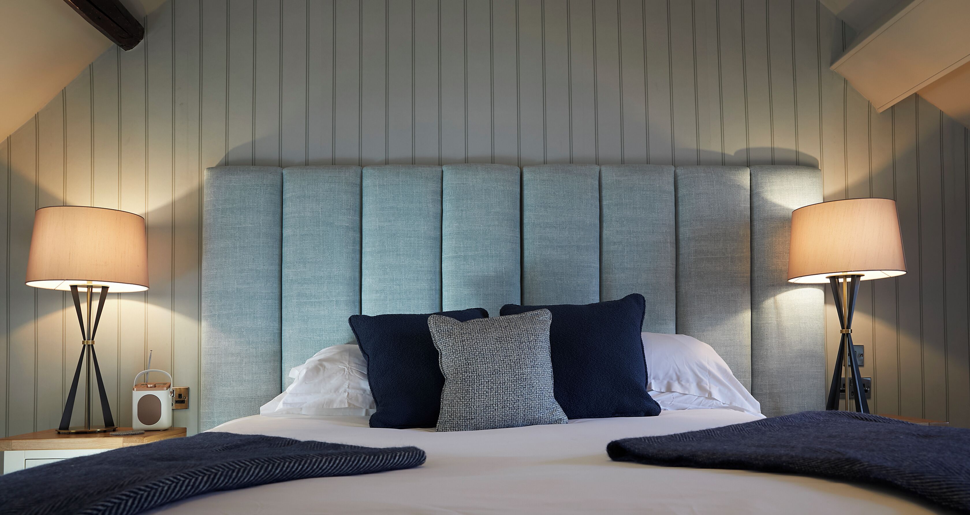 A neatly made bed with a headboard, two bedside lamps, and a radio on the nightstand.