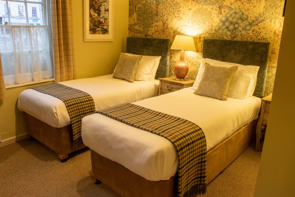 A hotel room with two single beds, each with a headboard, bedside tables, and lamps.