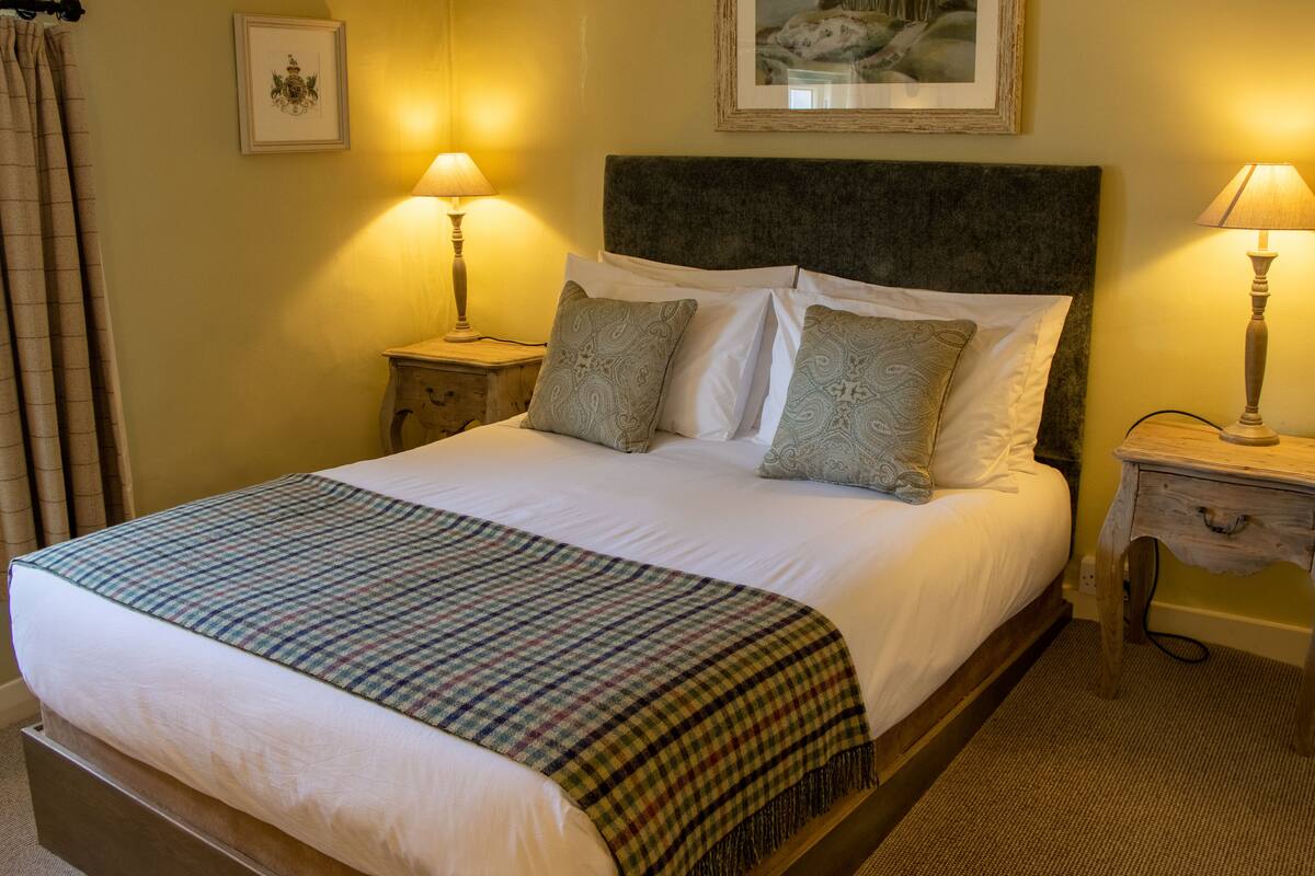 A neatly made bed with a plaid blanket, two bedside tables with lamps, and a framed picture on the wall.