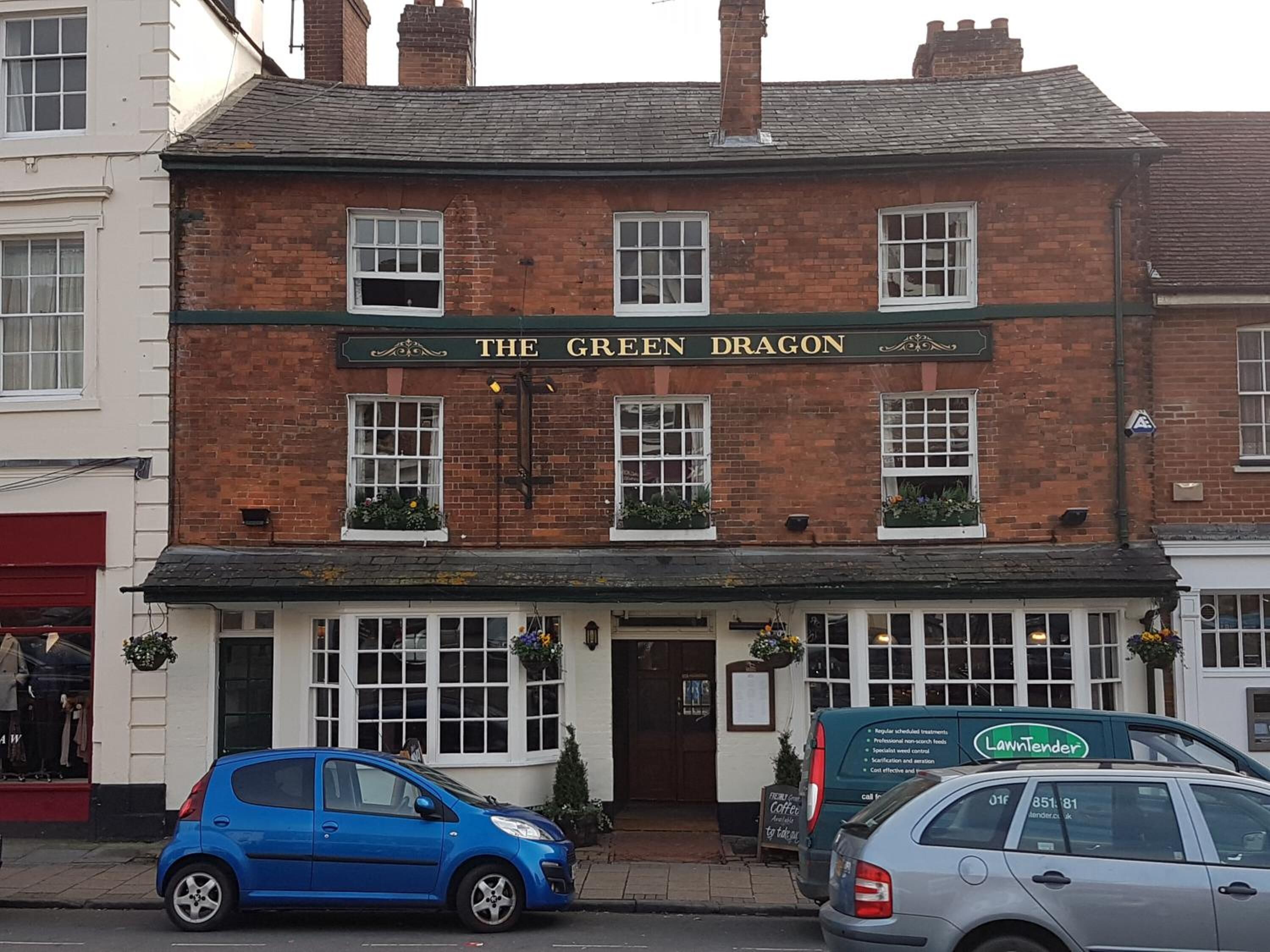 A traditional pub named "The Green Dragon" with a brick facade, white windows, and a green awning.