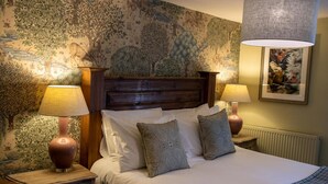Un dormitorio con cabecera de madera, dos lámparas de noche, un papel tapiz estampado y un cuadro en la pared.