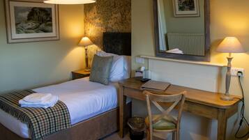 A hotel room with a bed, desk, chair, lamp, and a wall with a painting.