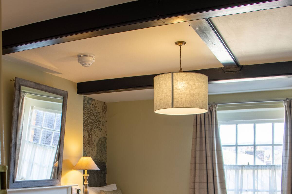 A hotel room with a bed, a desk, a chair, a lamp, and a window with curtains.