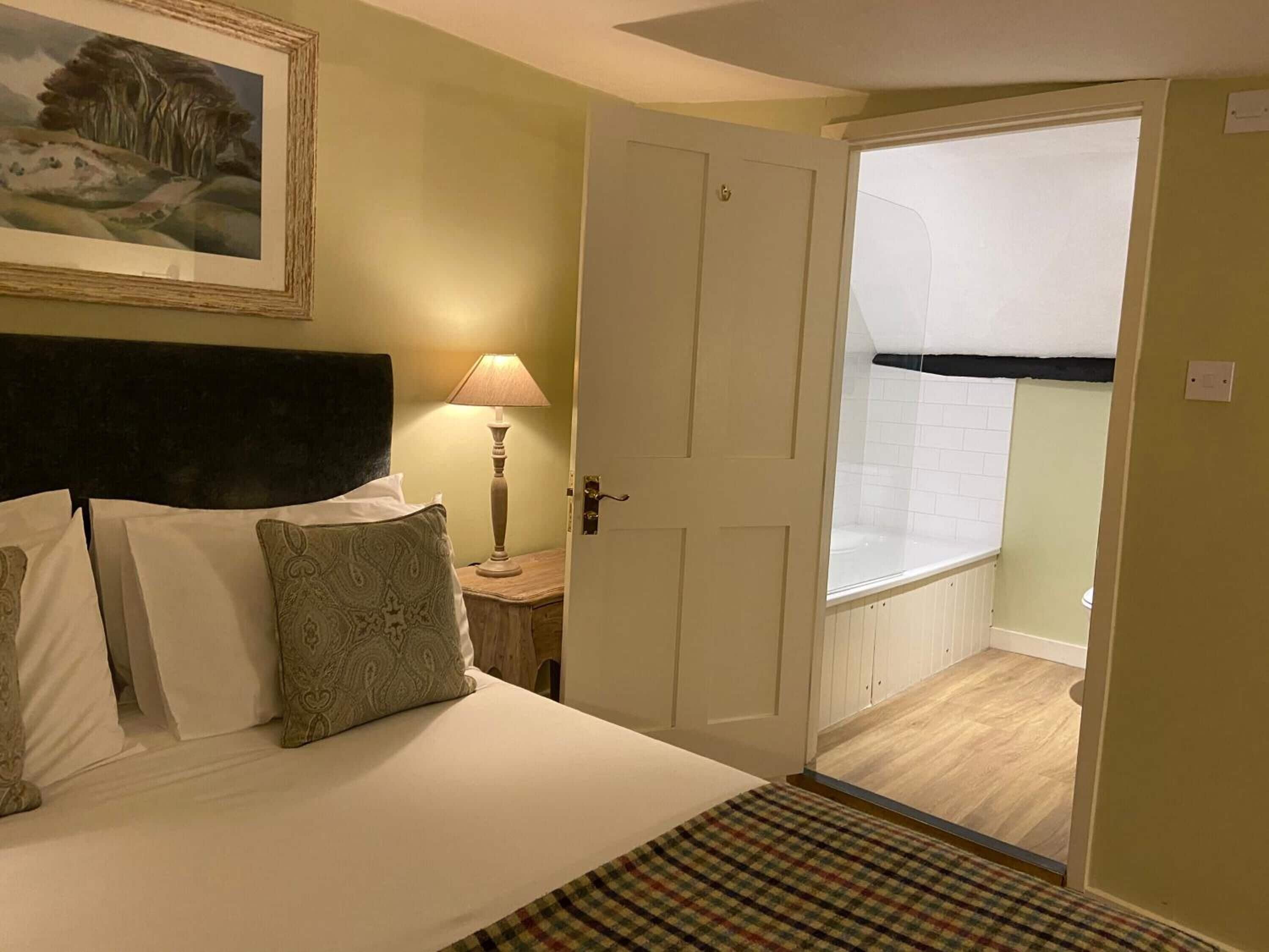 A bedroom with a bed, a nightstand, a lamp, a painting on the wall, and a door leading to a balcony.