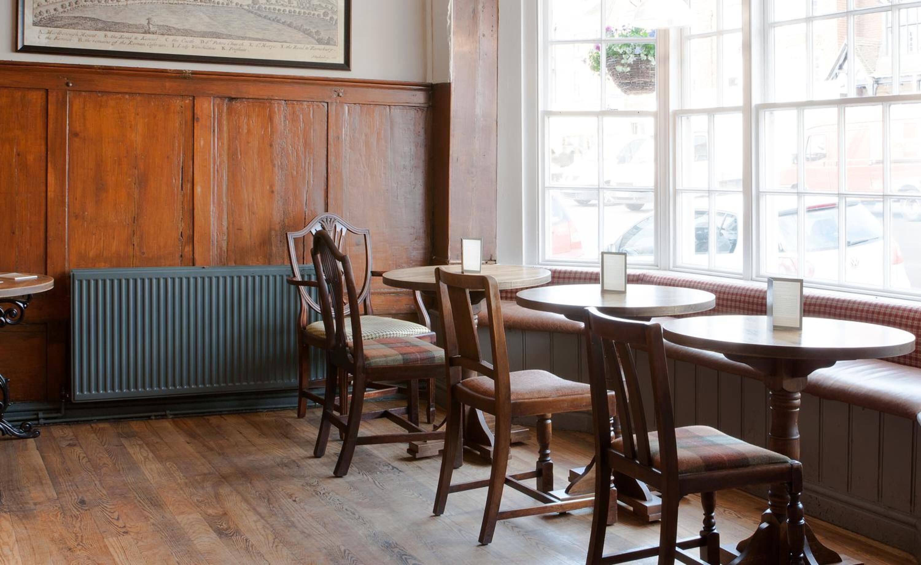A traditional inn with wooden paneling, a radiator, and a view of the street through large windows.