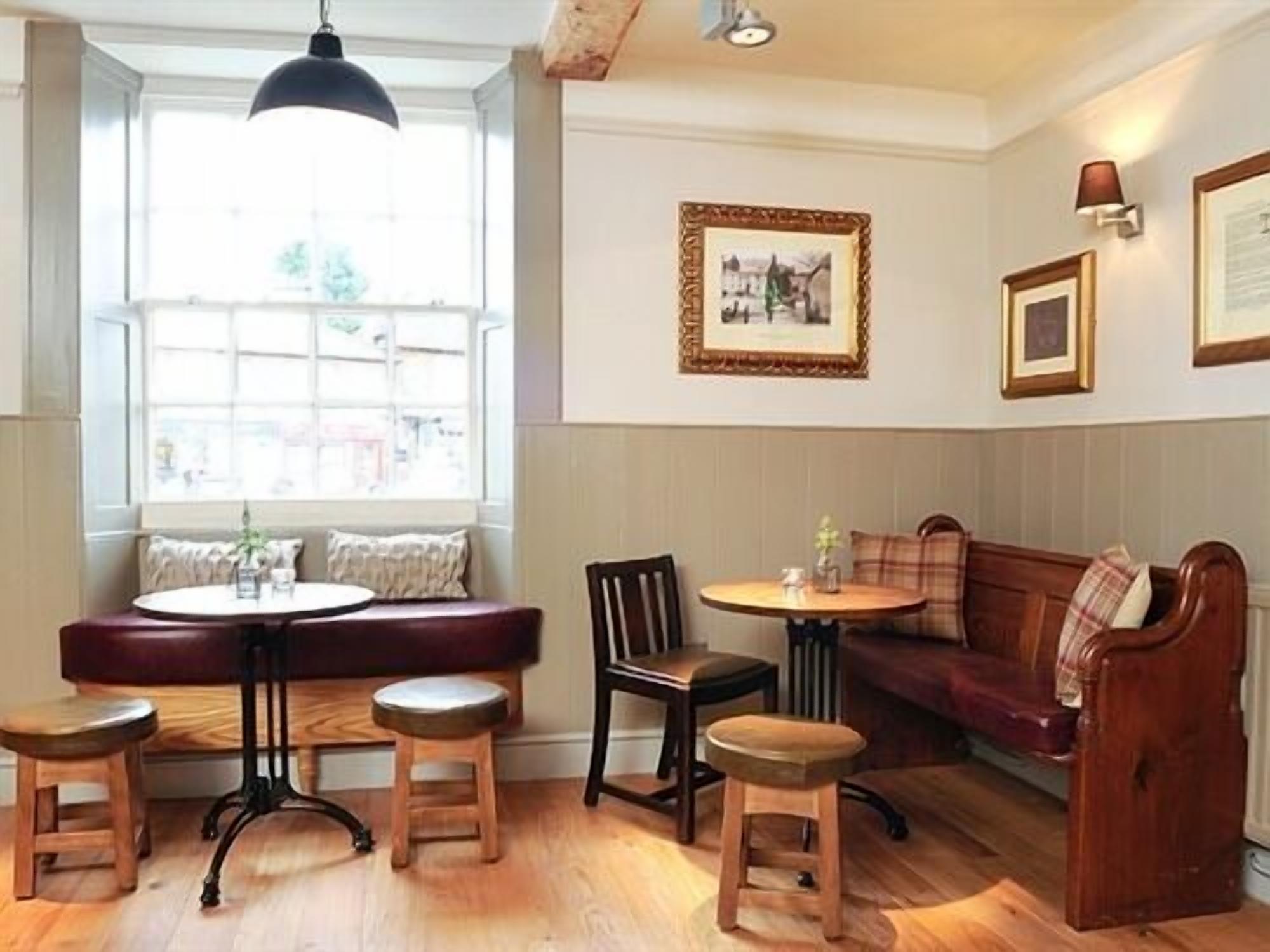 Una habitación acogedora con un banco de madera, dos taburetes, una mesa redonda y un sofá.