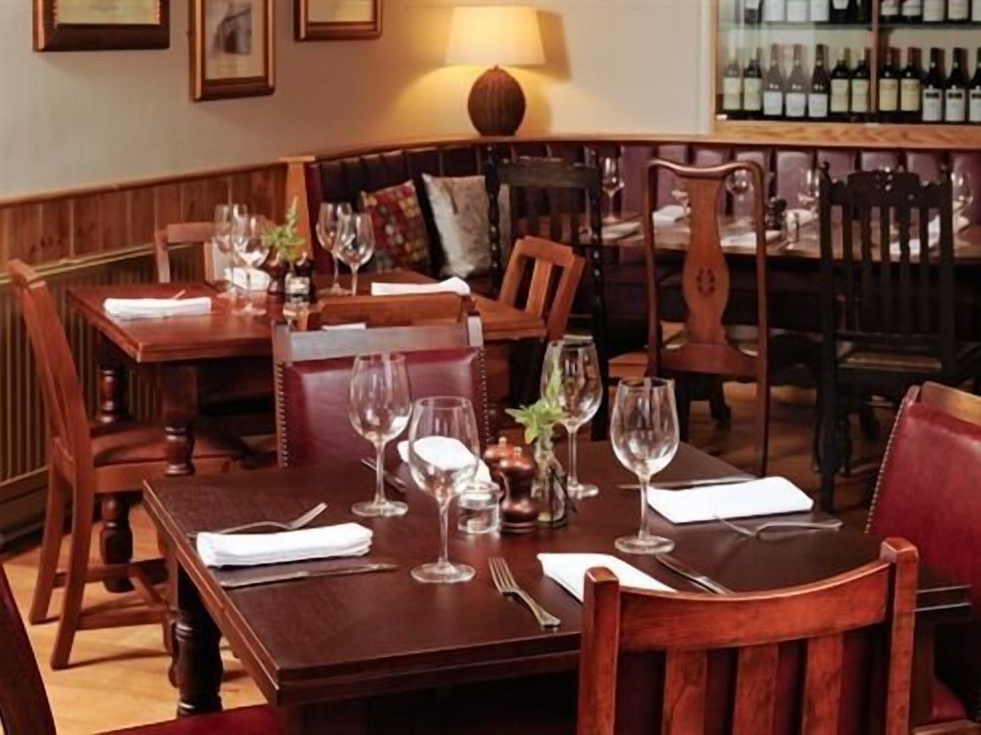 A dining area with wooden tables and chairs, wine glasses, and a bottle of wine on the table.