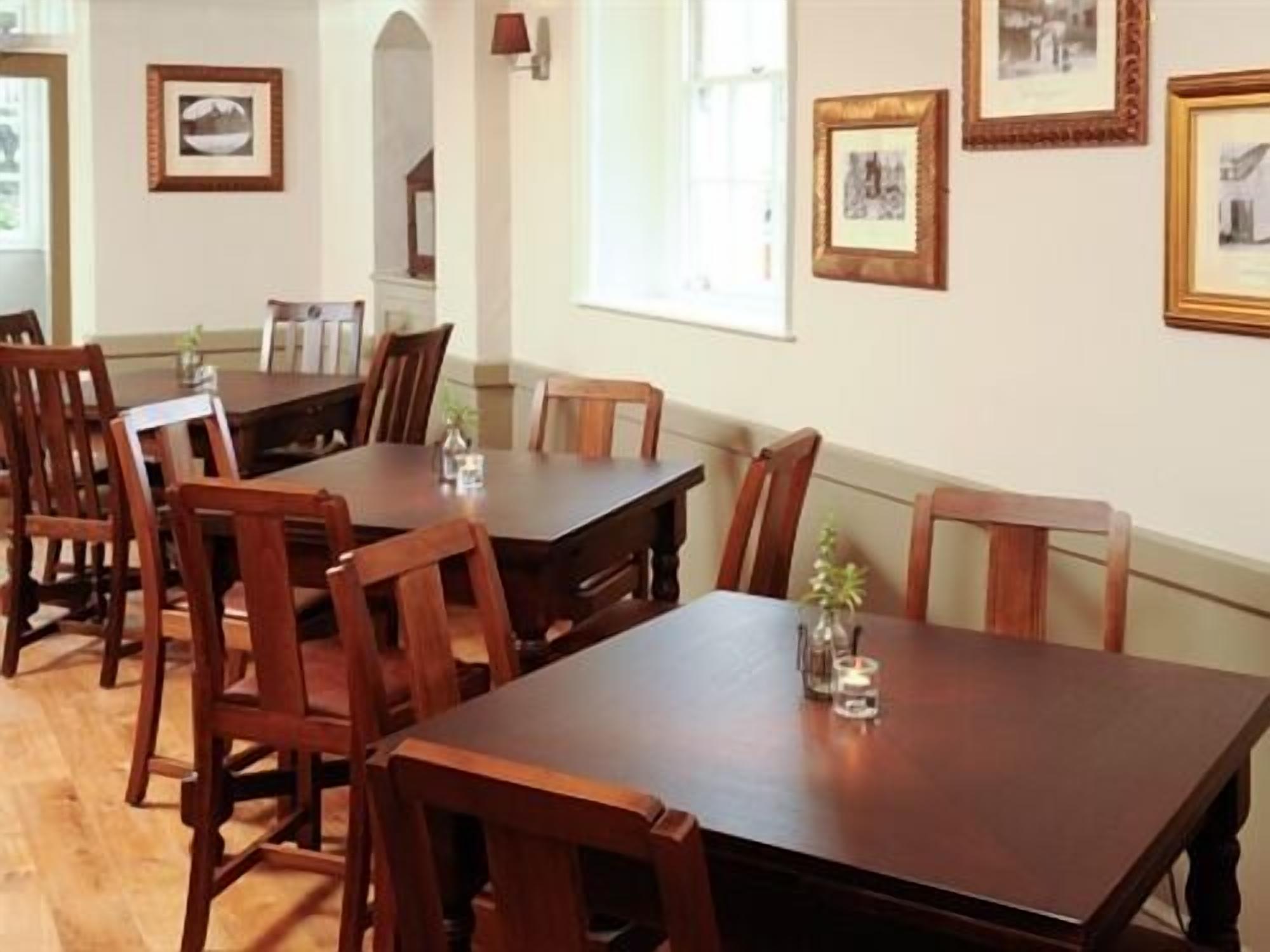 A dining area with wooden tables and chairs, framed pictures on the walls, and a window providing natural light.