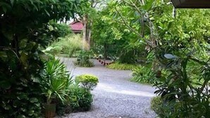 A pathway leading through a lush garden area with various plants and a red-roofed building in the background. - Bangyai Buri Resort (Surat Thani)