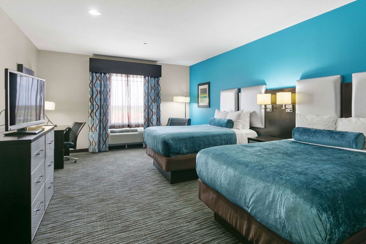 A hotel room with two beds, a desk, a television, and a window with curtains.