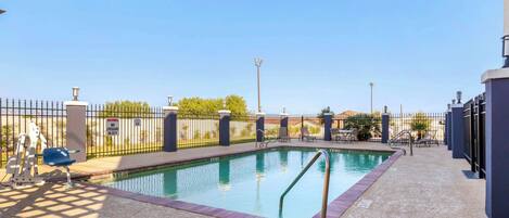 Una piscina con borde de baldosas, cerca de metal y sillas de descanso.