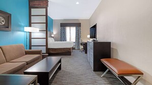 Une chambre d’hôtel équipée d’un lit, d’un canapé, d’un bureau, d’une banquette, d’une télévision et d’une lampe de bureau.