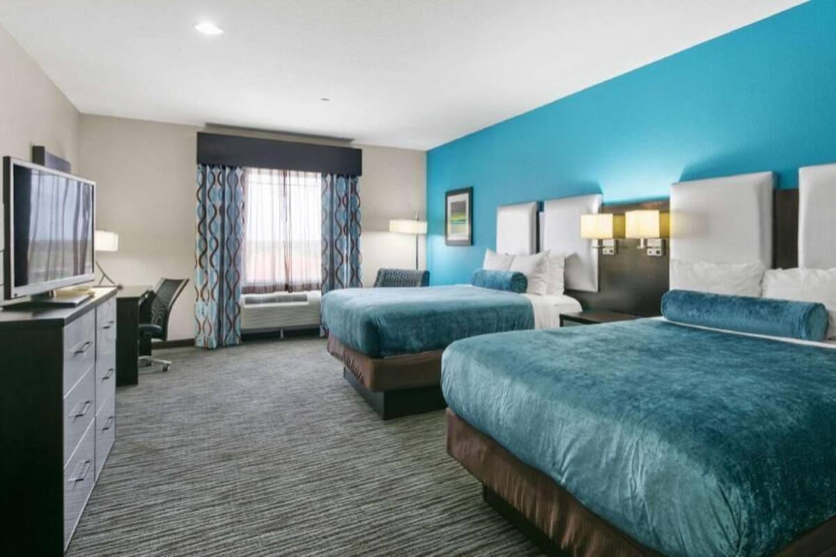 A hotel room with two beds, a desk, a television, and a window with curtains.