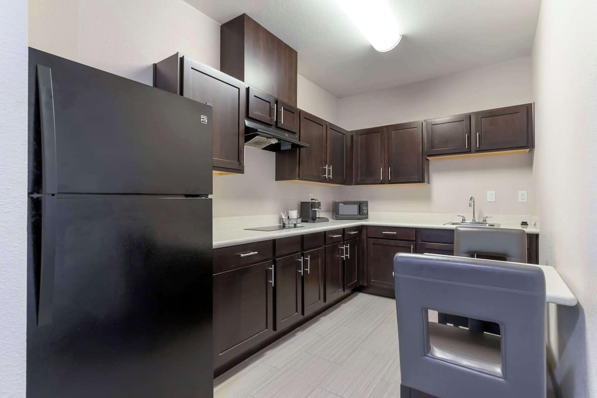A modern kitchen with dark wooden cabinets, a black refrigerator, a microwave, and a sink.