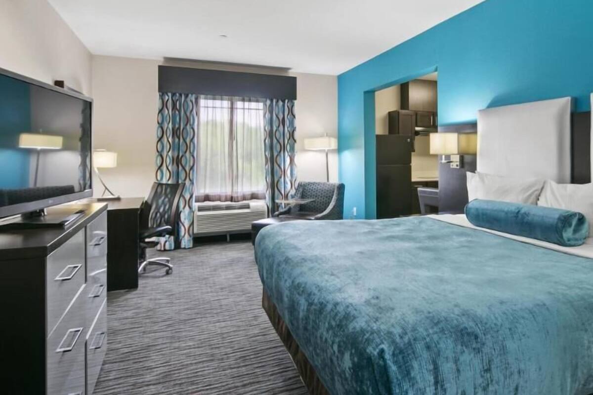 A hotel room with a bed, a TV, a desk, a chair, and a window with curtains.