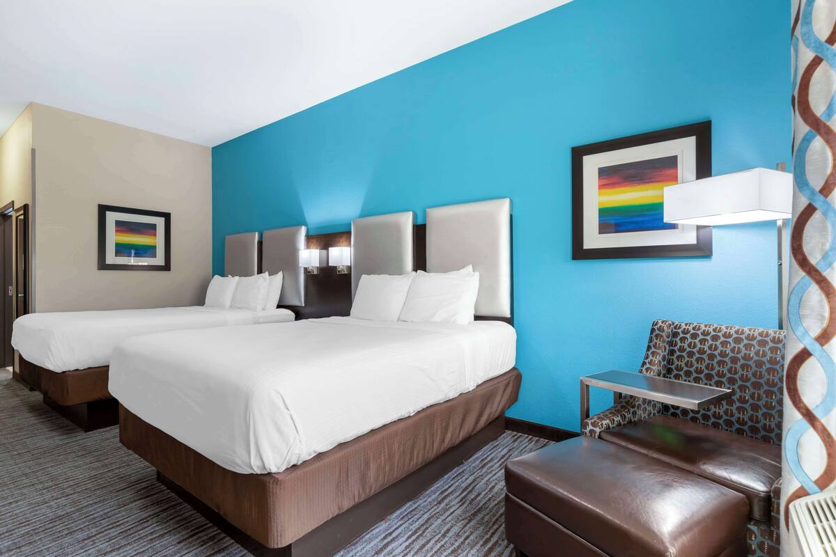 A hotel room with two beds, a small table, a chair, and a lamp.