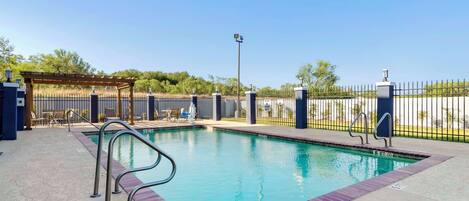 A swimming pool with a metal ladder, a covered seating area, and a fenced patio with chairs and tables.
