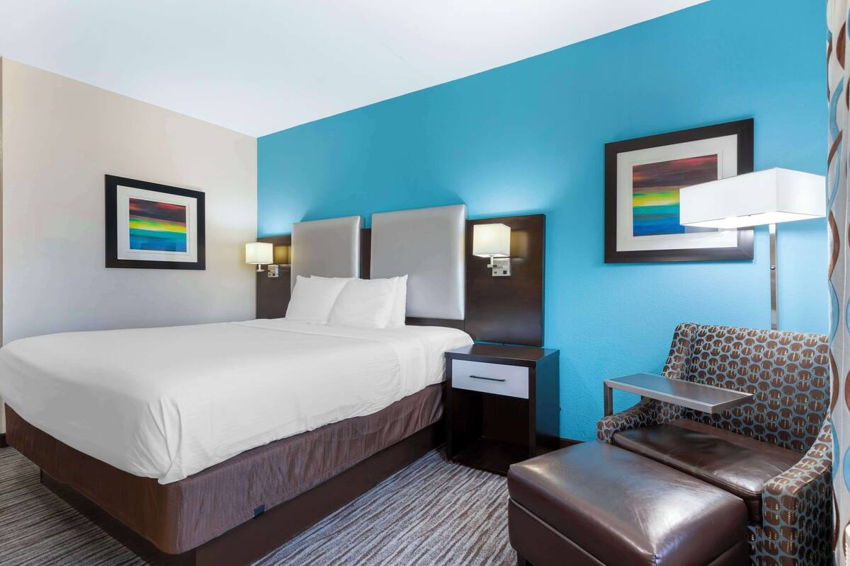A hotel room with a large bed, bedside tables, a chair, and artwork on the walls.