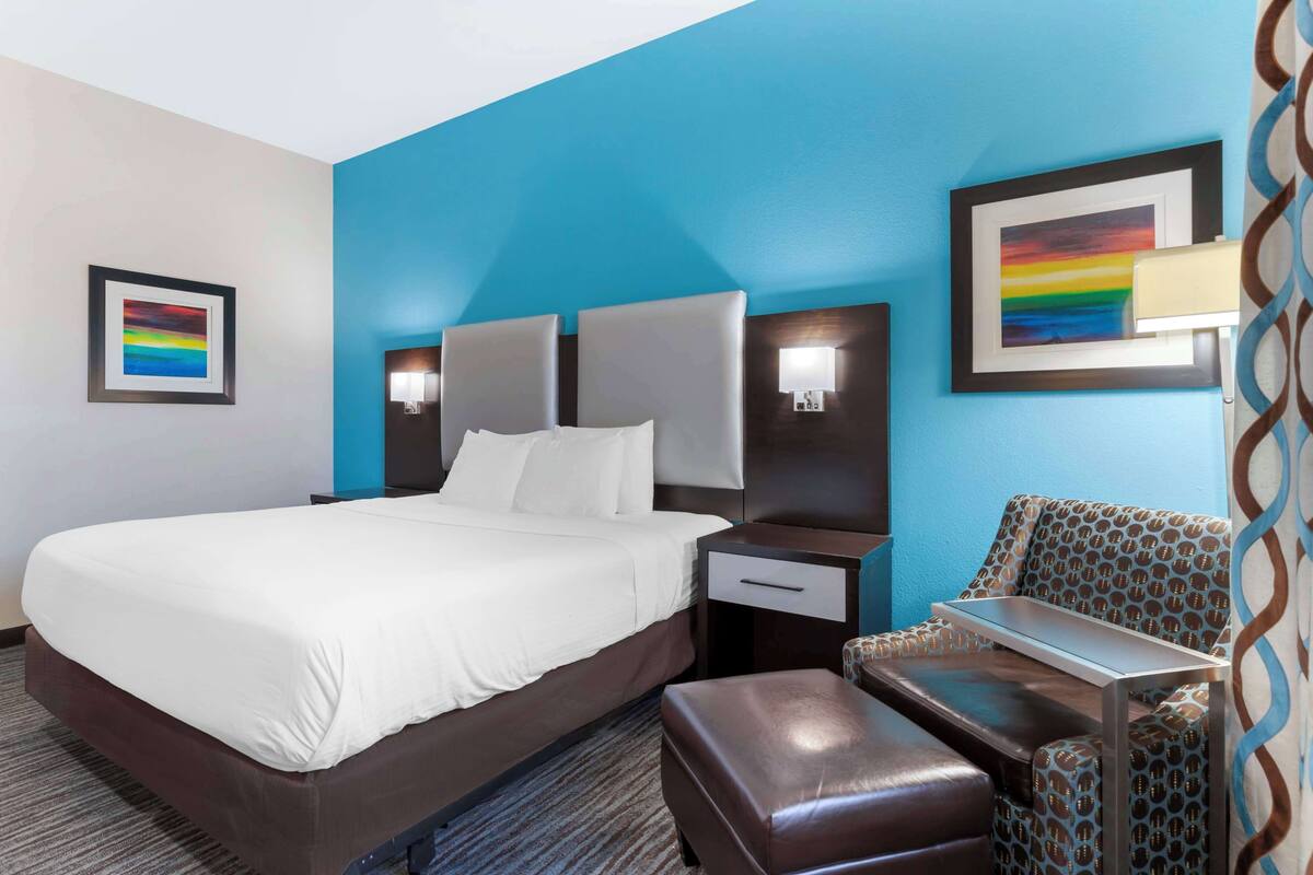 A hotel room with a large bed, a nightstand, a chair, and a desk.