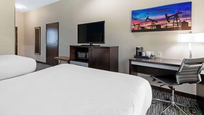 Une chambre d’hôtel avec deux lits, une télévision, un bureau avec une chaise, un four à micro-ondes et un tableau représentant des pompes à pétrole accroché au mur.