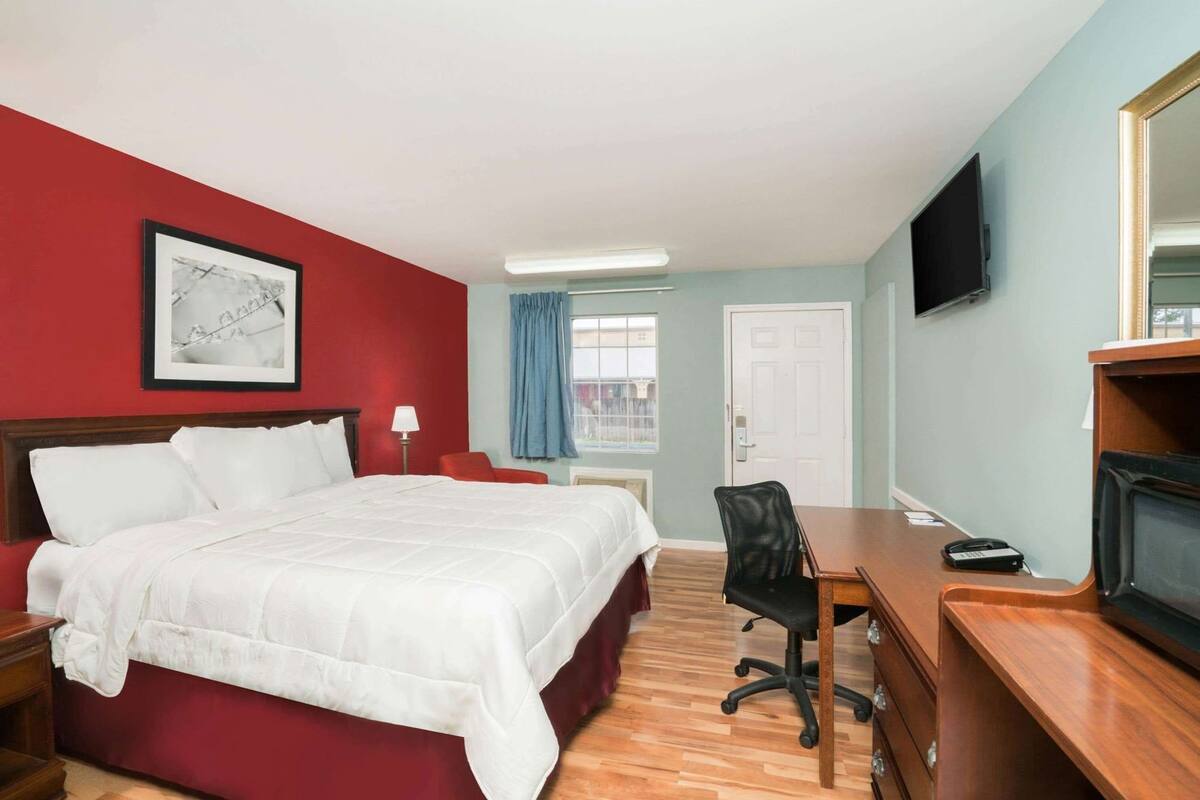 Une chambre d’hôtel avec un lit, un bureau, une chaise, une télévision et un tableau encadré au mur.