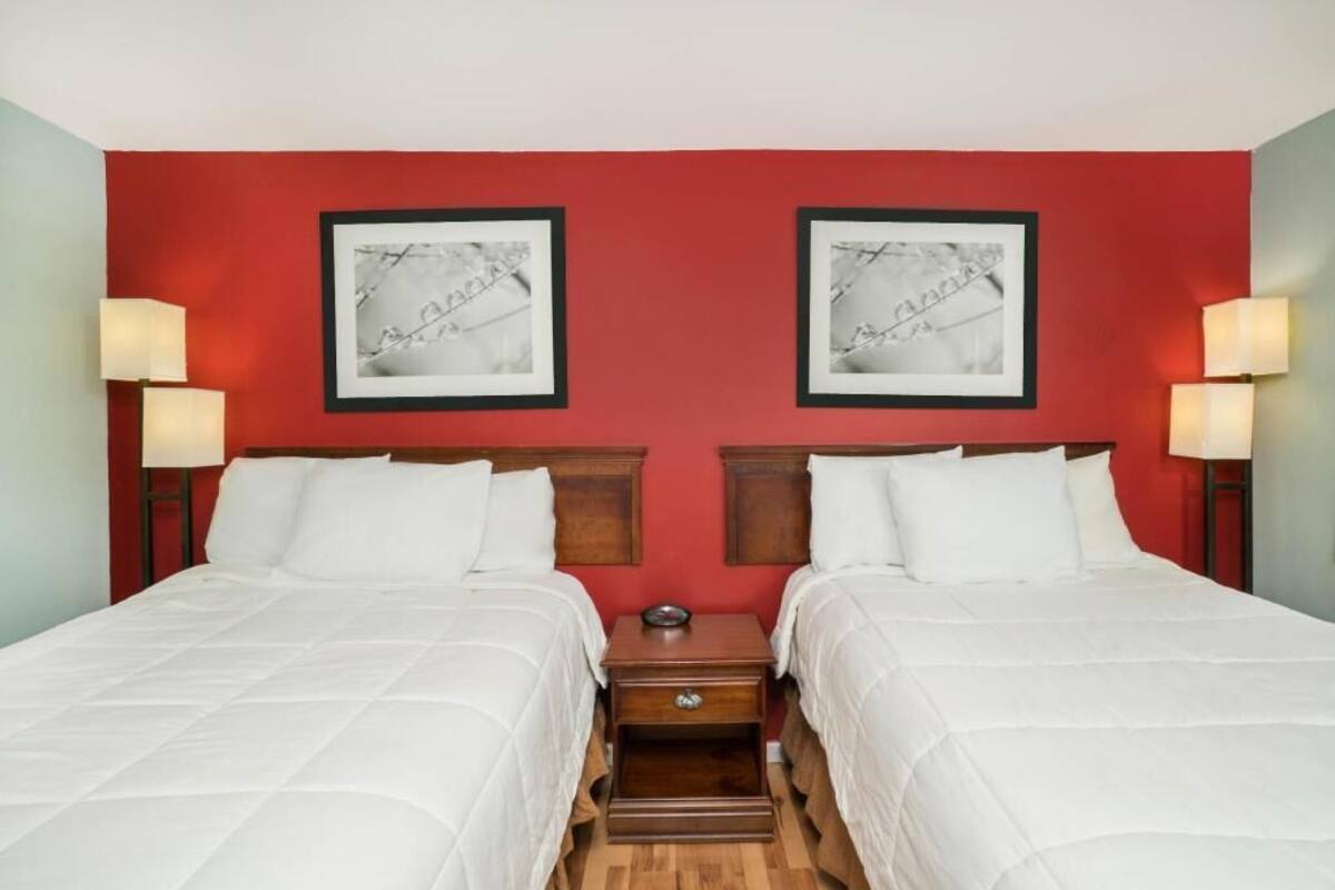 Une chambre d’hôtel avec deux lits, un mur d’accent rouge, des œuvres d’art encadrées, des lampes de chevet et une petite table de chevet.