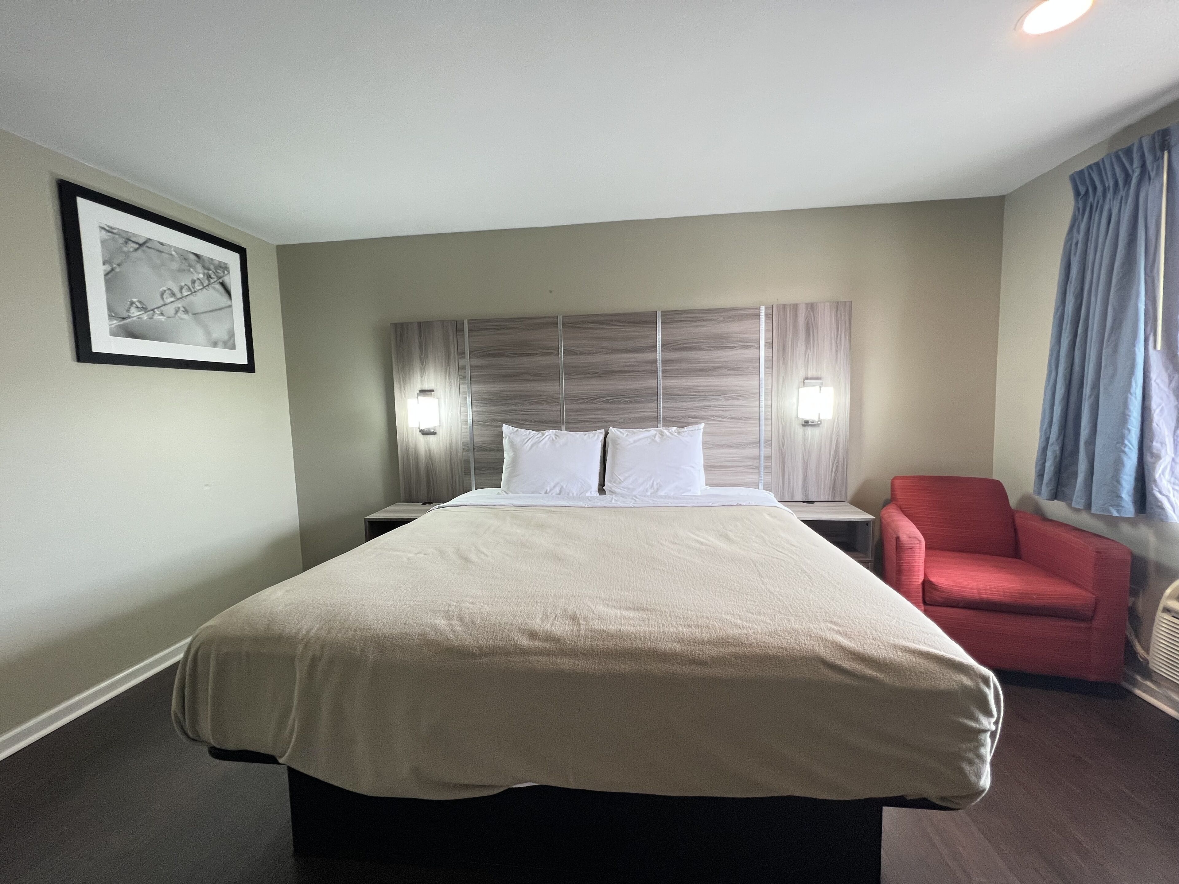 A hotel room with a large bed, two bedside tables, a red chair, and a framed picture on the wall.
