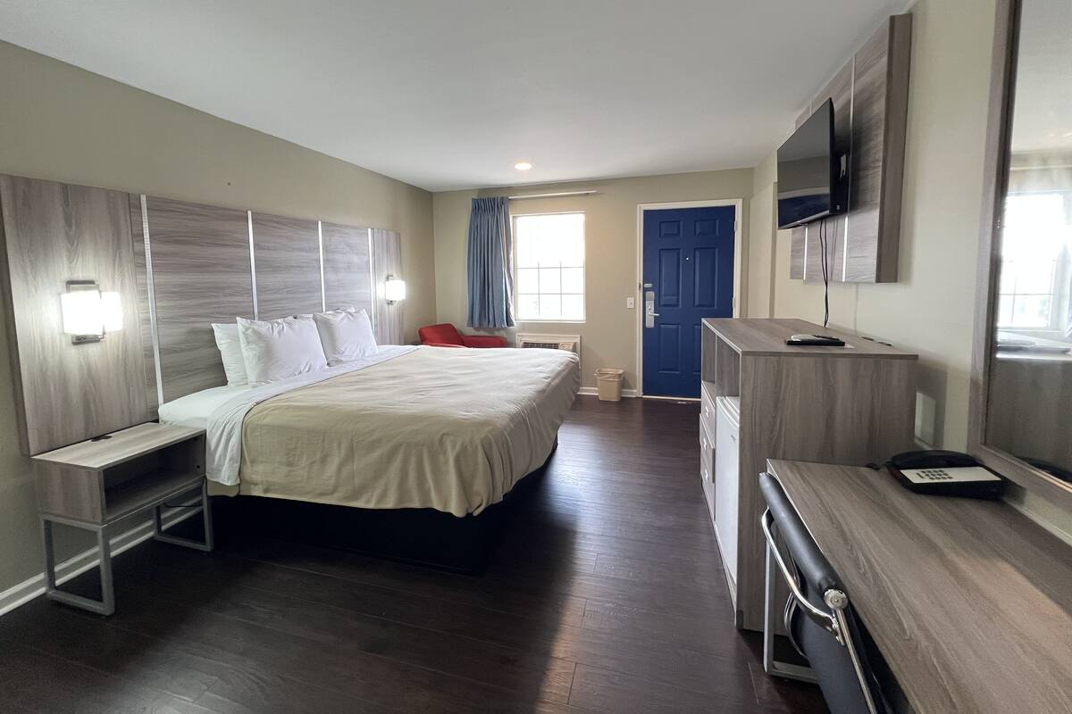 Une chambre d’hôtel avec un grand lit, des tables de chevet, un bureau, une chaise, une télévision et une porte.