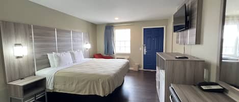 Quarto de hotel com uma cama grande, mesas de cabeceira, uma escrivaninha, uma cadeira, televisão e uma porta.