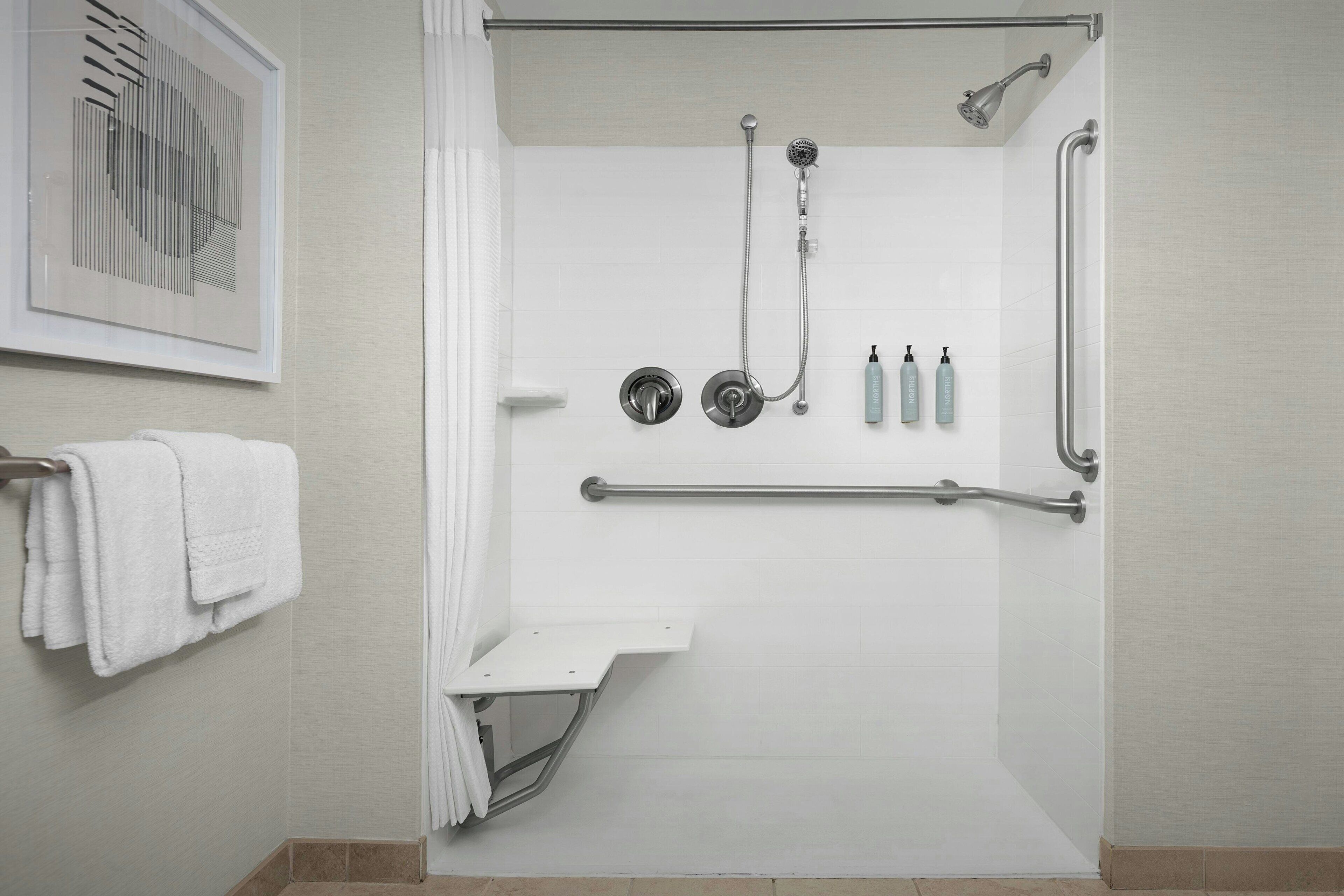 A modern bathroom with a walk-in shower, grab bars, and a towel rack.