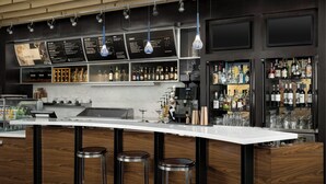 Una zona de bar moderna con una barra curva, detalles de madera y lámparas colgantes.