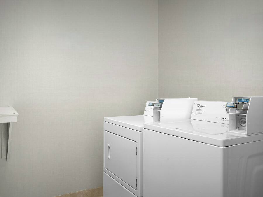 A laundry area with two stacked washing machines and a white shelf.