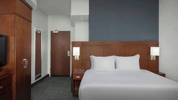 Een hotelkamer met een groot bed, een houten hoofdeinde, twee nachtkastjes met lampen, een garderobe en een televisie.