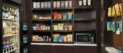 Una kitchenette equipada con refrigerador, microondas y estantes llenos de aperitivos y bebidas.