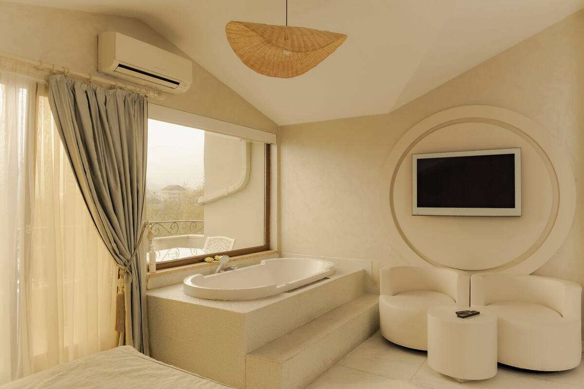 A modern bathroom with a bathtub, a large mirror, a television mounted on the wall, and a wicker ceiling light.