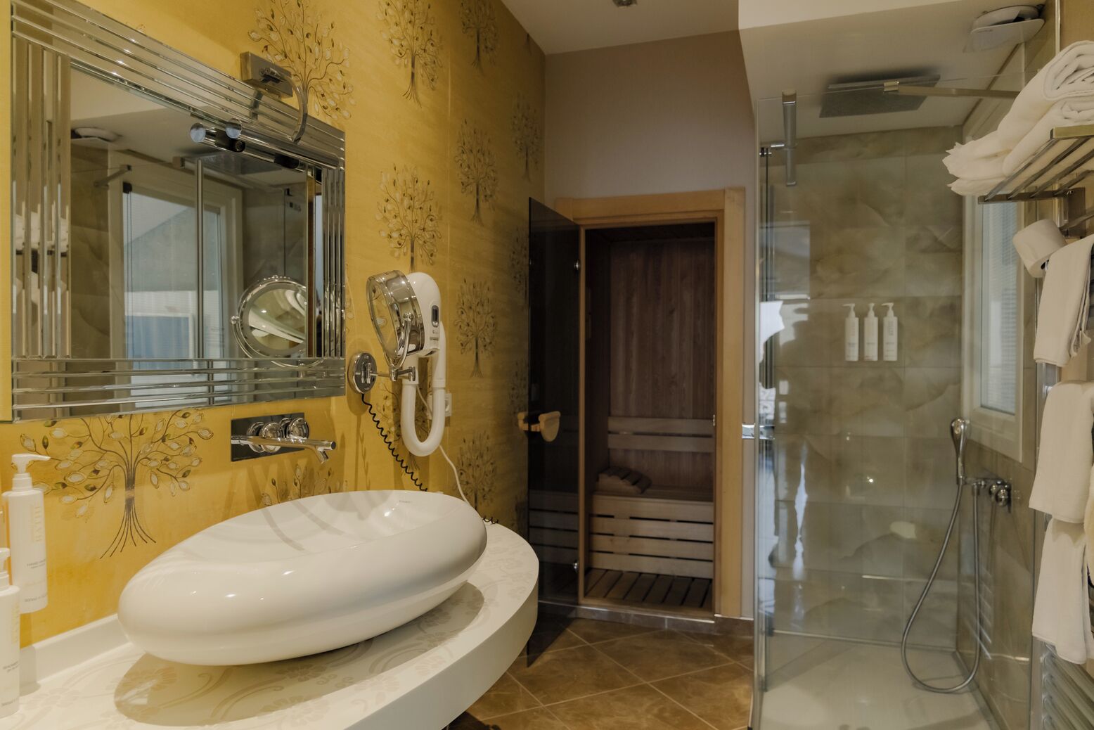 A bathroom with a large oval sink, a glass shower enclosure, and a wooden door leading to a sauna.