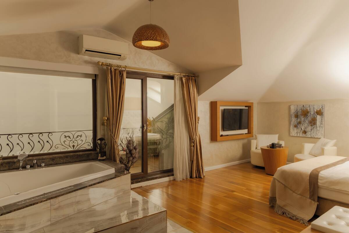 A modern bedroom with a large bed, a bathtub, and a sliding glass door leading to a balcony.