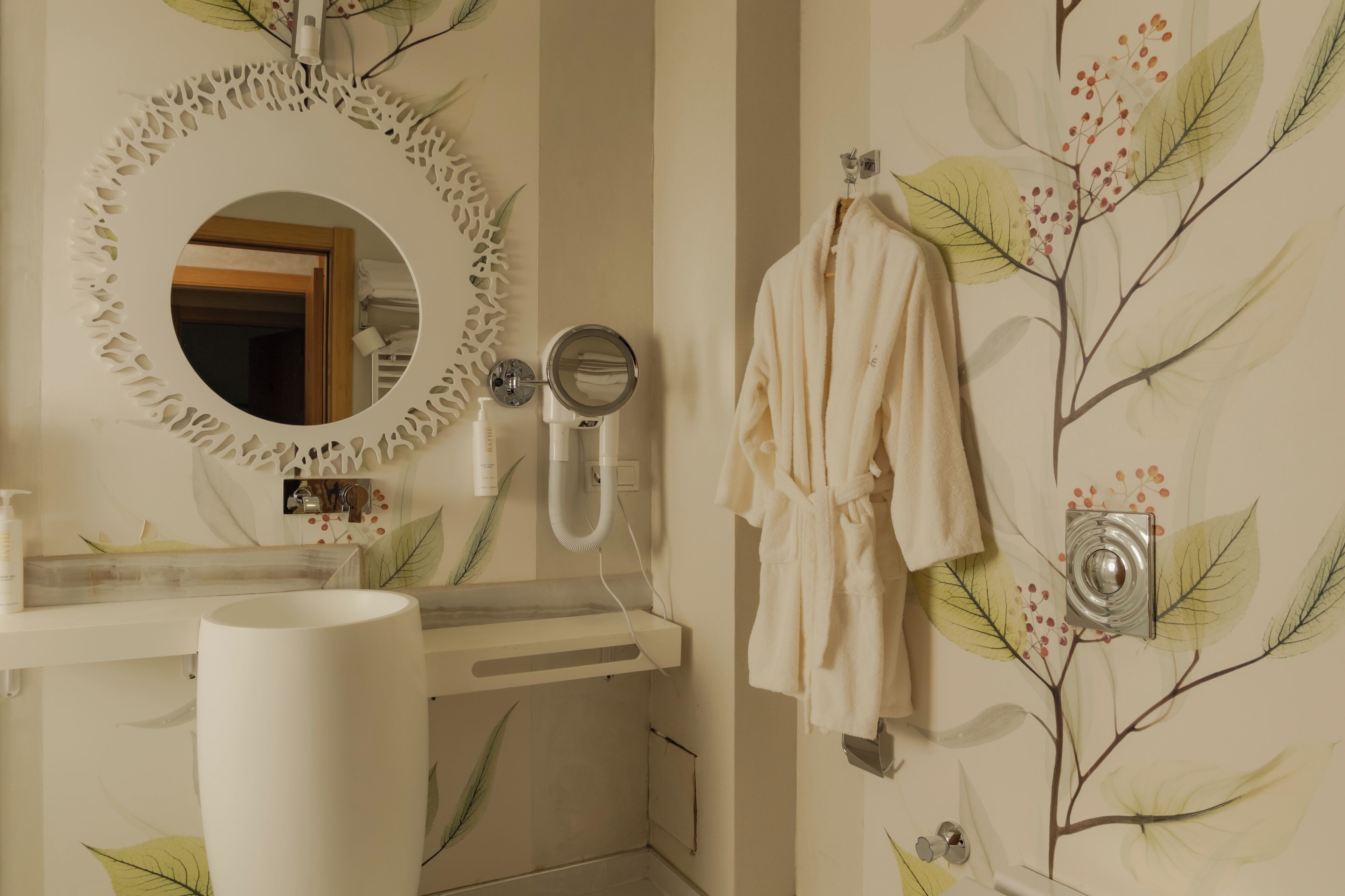 A bathroom with a round mirror, a towel rack, a sink, and a wall-mounted camera.