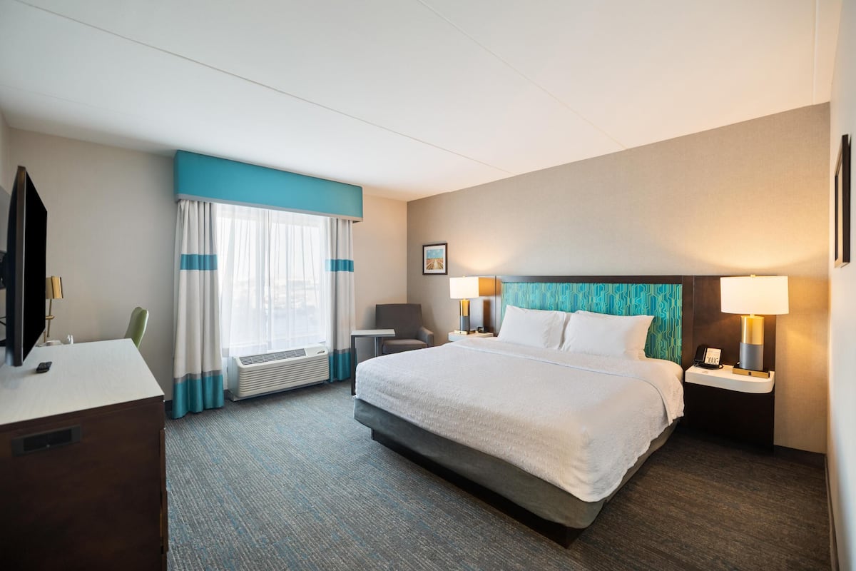 Ein Hotelzimmer mit Bett, Nachttischen, Schreibtisch, Stuhl, Fernseher und einem Fenster mit Vorhängen.
