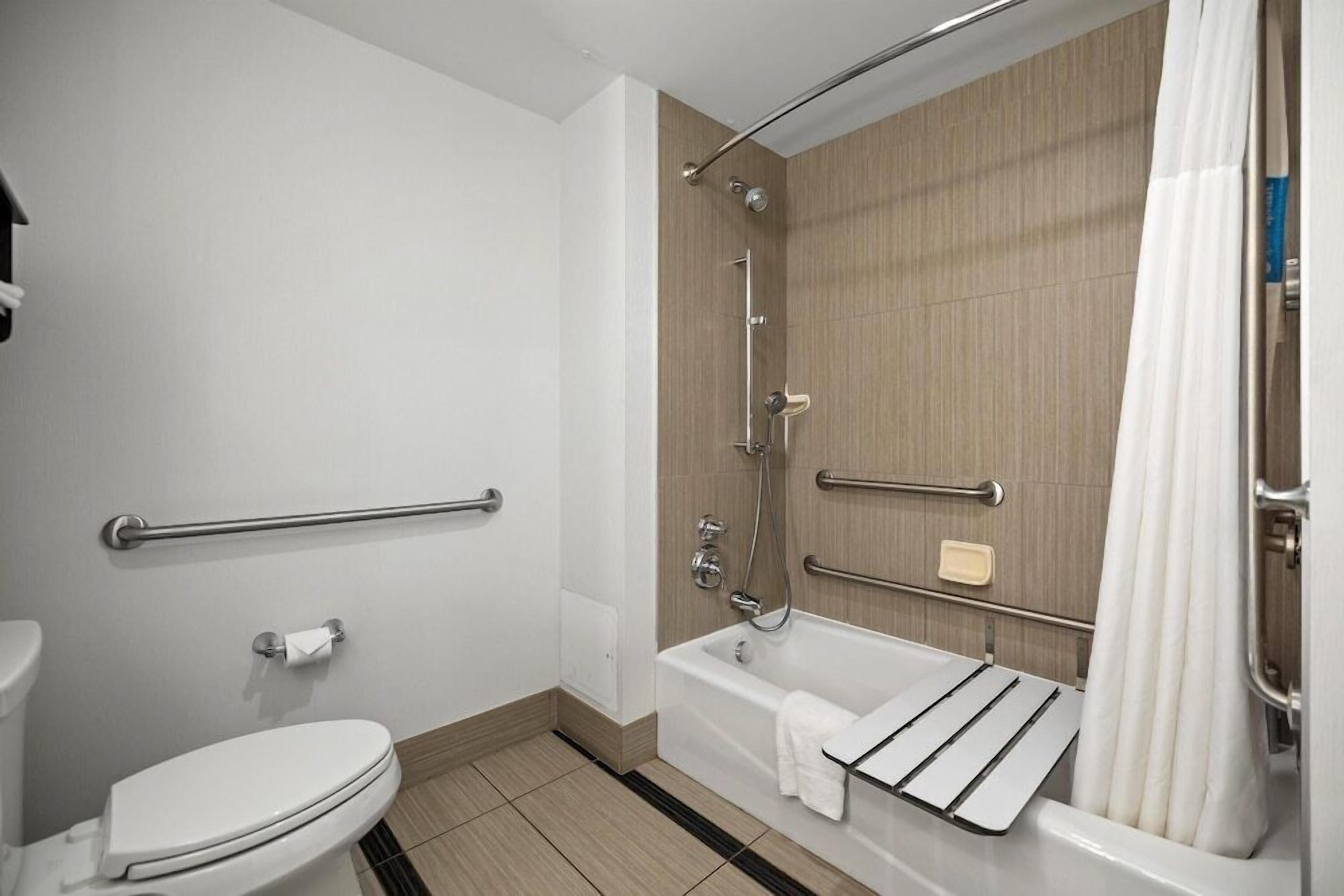 Un baño moderno con inodoro, ducha con barra de apoyo y bañera con perchero para toallas.