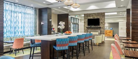 A modern bar area with a long counter, multiple stools, and a television mounted on a stone wall.