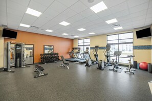 Une salle de sport équipée de tapis de course, de vélos elliptiques, de poids libres et d’une machine de musculation.