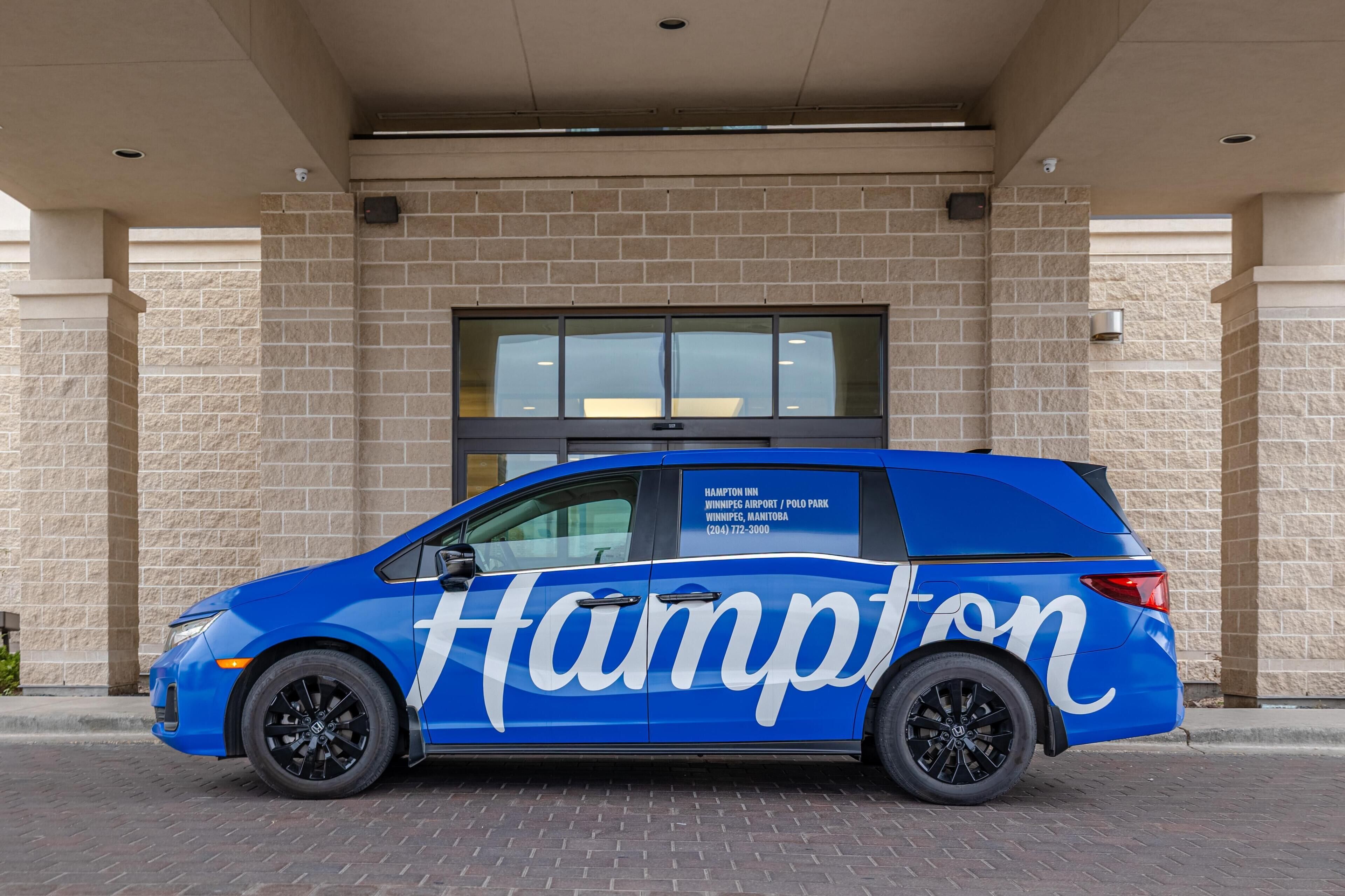 A blue van with 'Hampton' branding parked in front of a building with a brick facade and large windows.