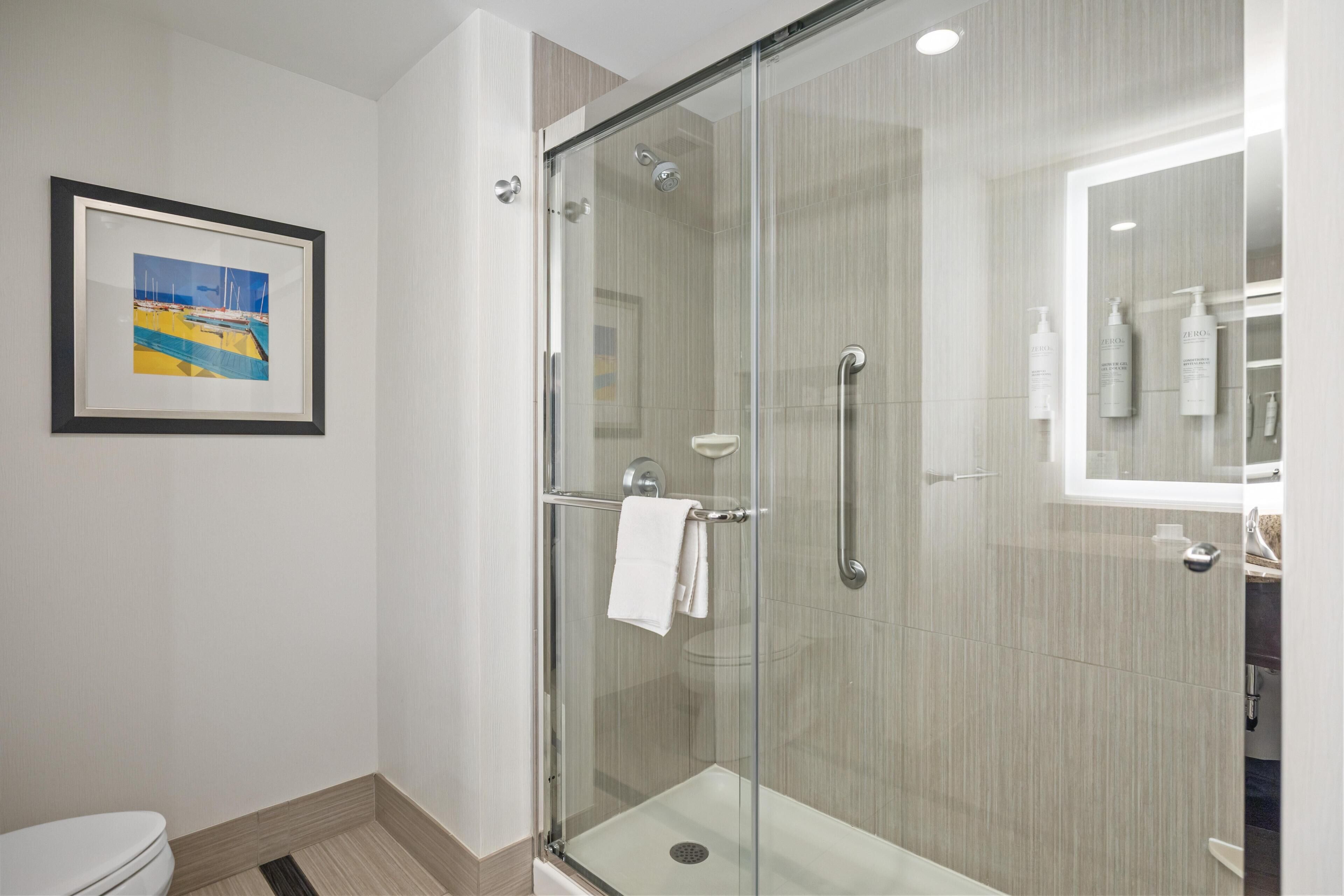 A modern bathroom with a glass shower enclosure, a framed picture on the wall, and toiletries on the counter.
