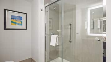 Een moderne badkamer met een douchecabine van glas, een ingelijst schilderij aan de wand en toiletartikelen op het aanrecht.