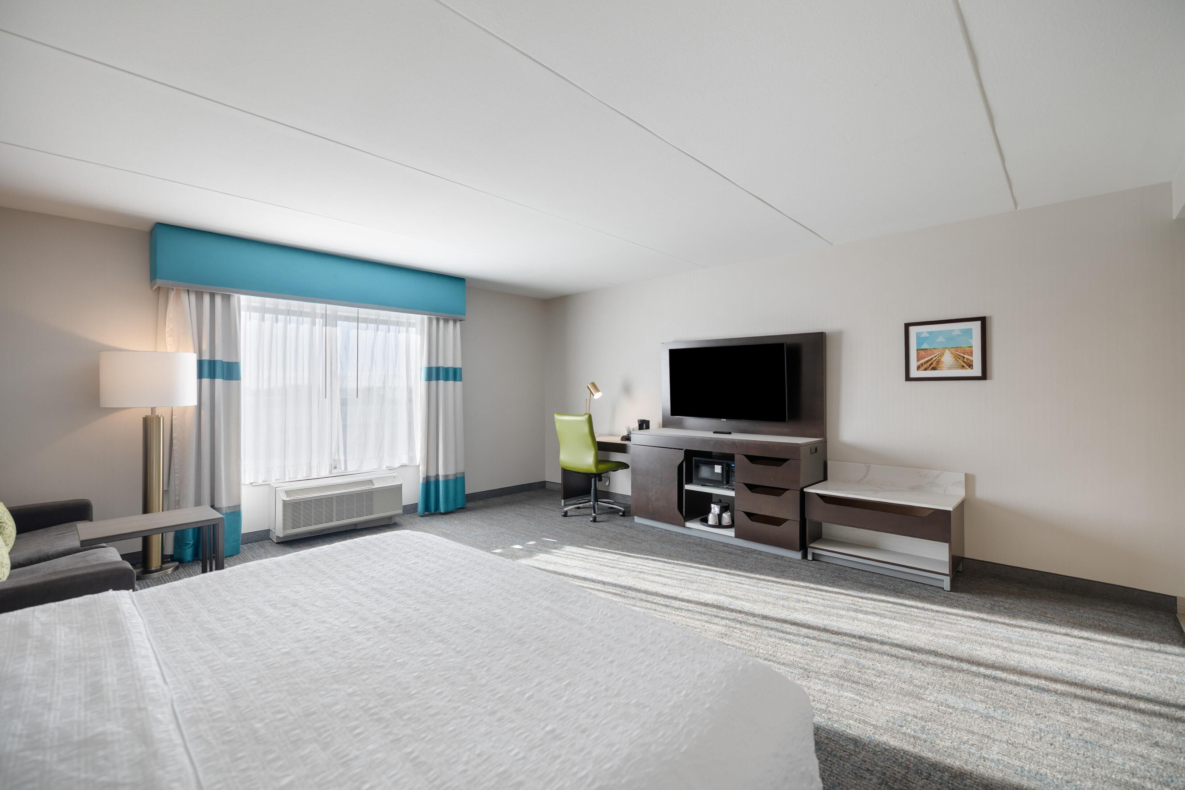 A hotel room with a bed, a desk, a television, a chair, and a picture on the wall.