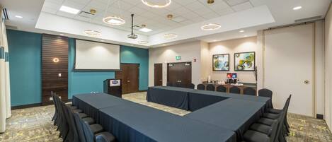 A conference room with a long table, chairs, a podium, and a projector screen.
